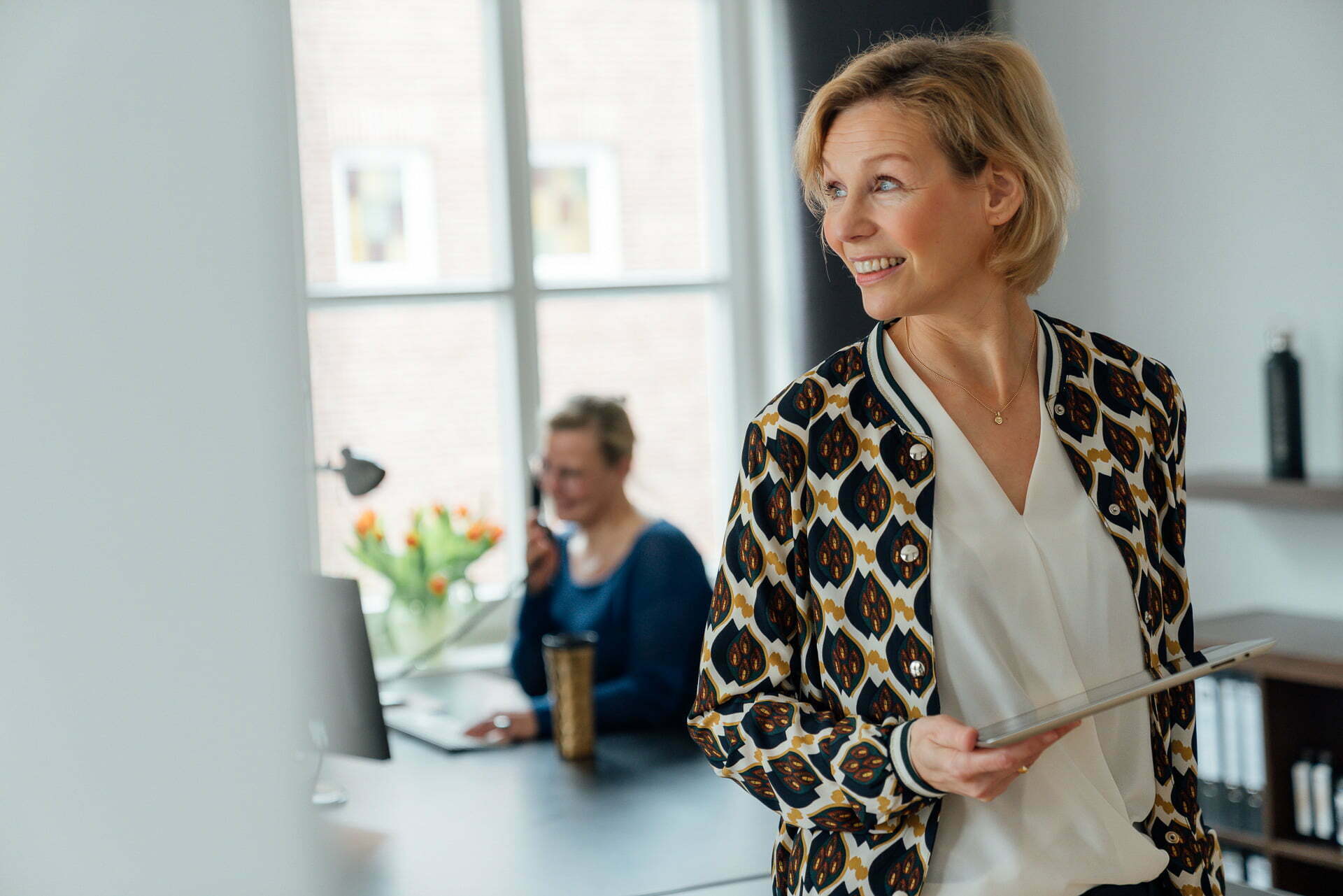 Beispiel-Personal-Branding-Fotografie Frau steht mit einem Tablet in der Hand vor einem Schreibtisch