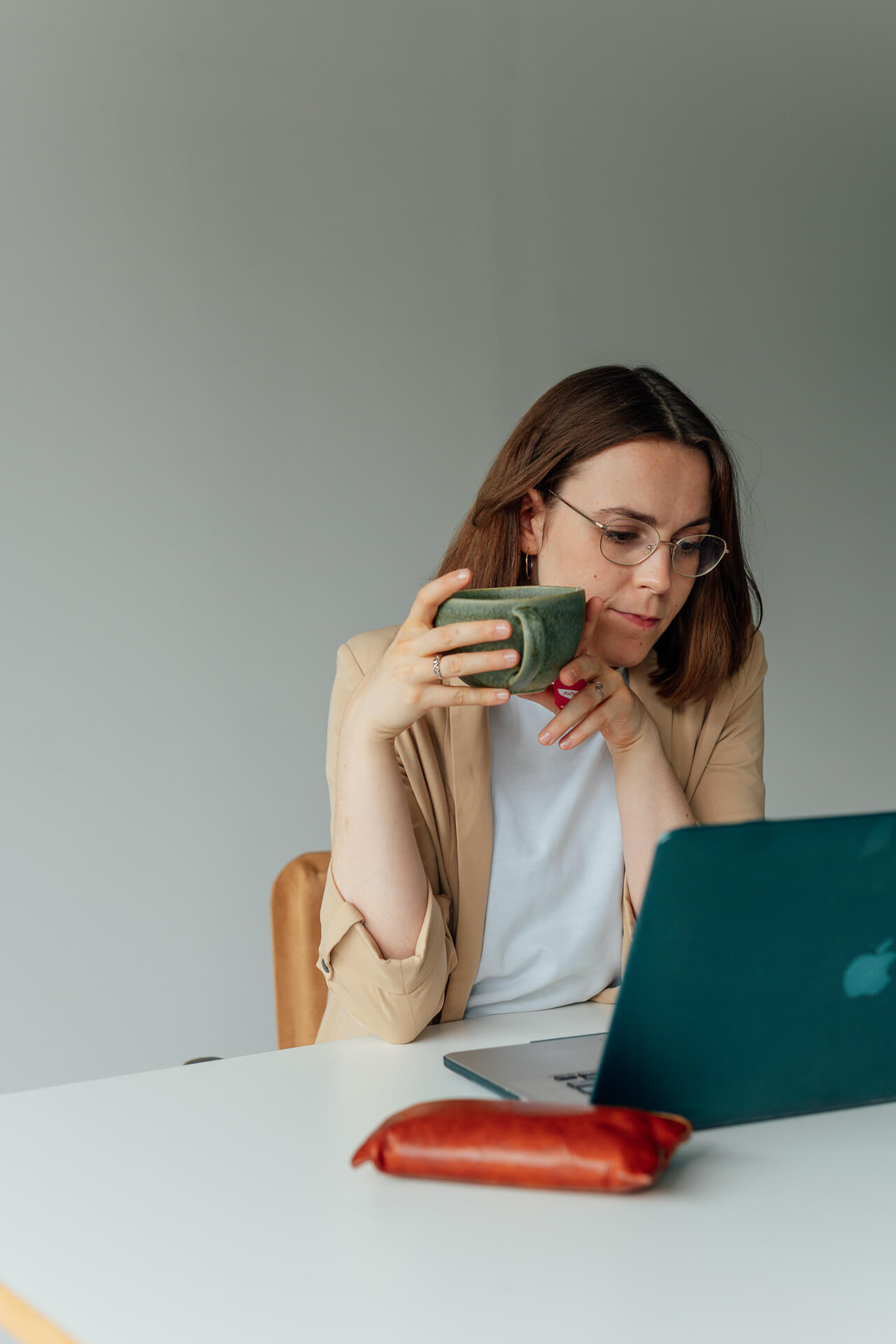 Portrait einer Frau die am Schreibtisch sitzt, sie hat dabei eine Tasse in der Hand und schaut in den Laptop. Das Bild ist während eines Brand Shoots entstanden. 