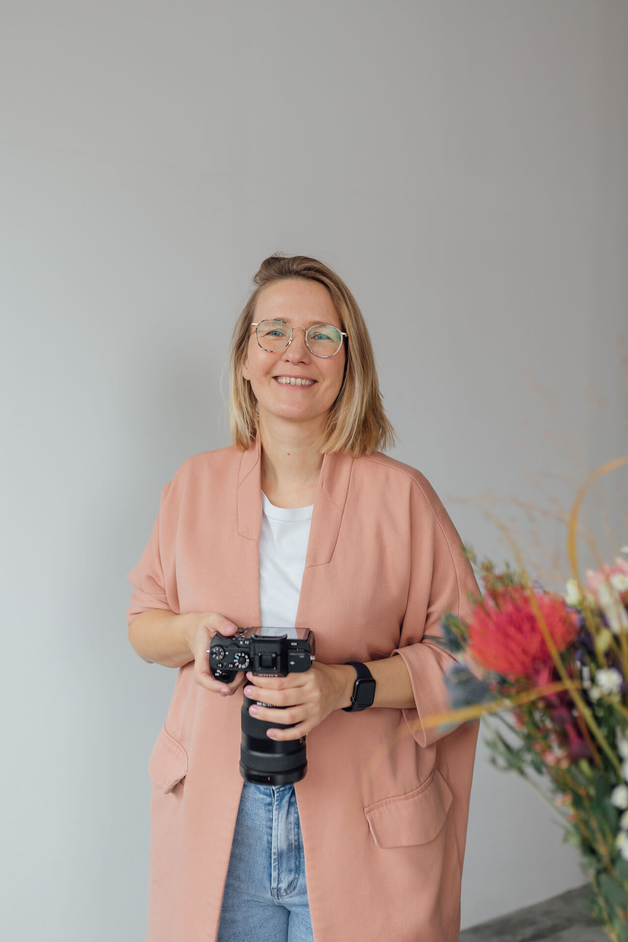 Businessfotografin Mirjam Kilter steht mit einer Kamera in der Hand und lächtelt