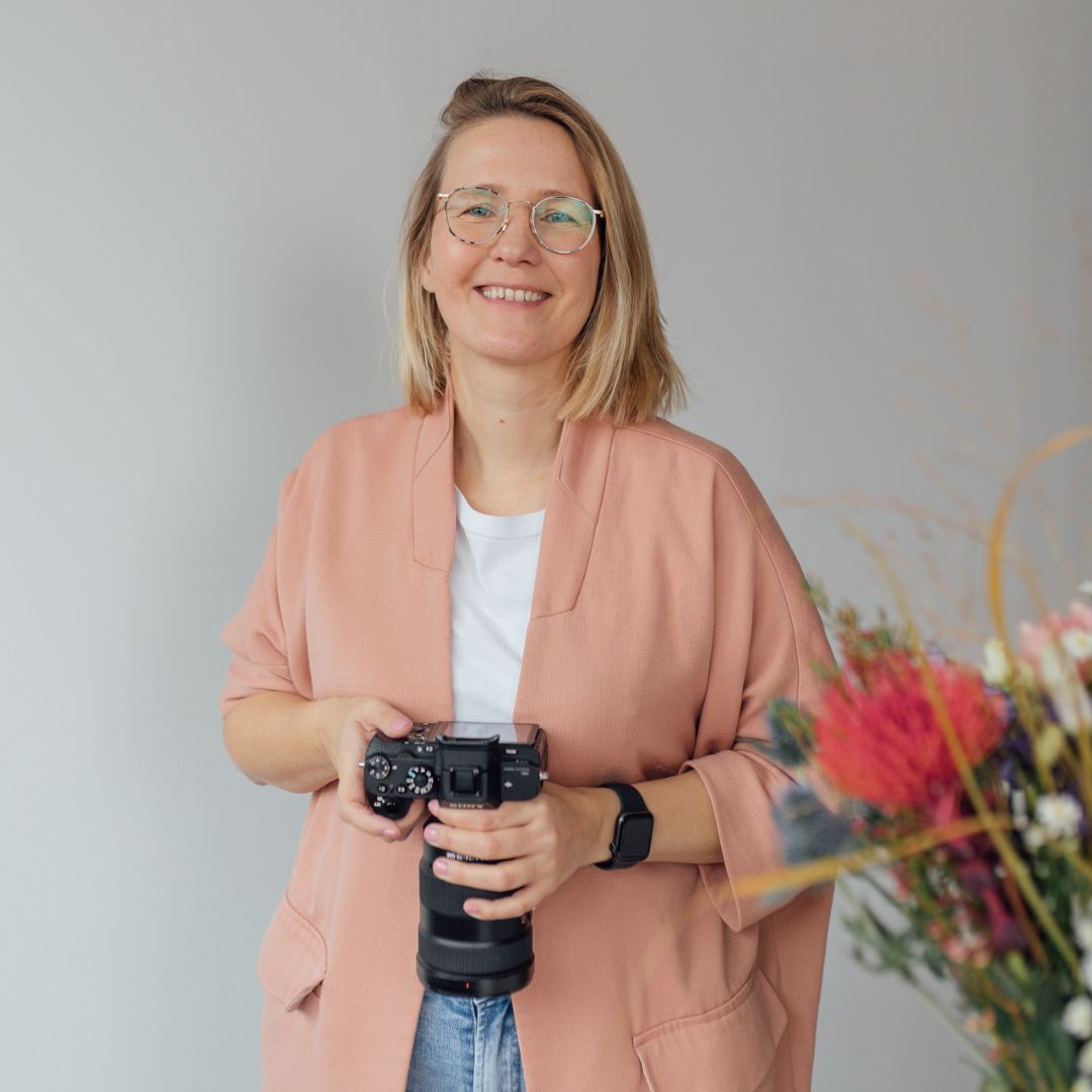 Businessfotografin Mirjam Kilter steht mit einer Kamera in der Hand und lächtelt