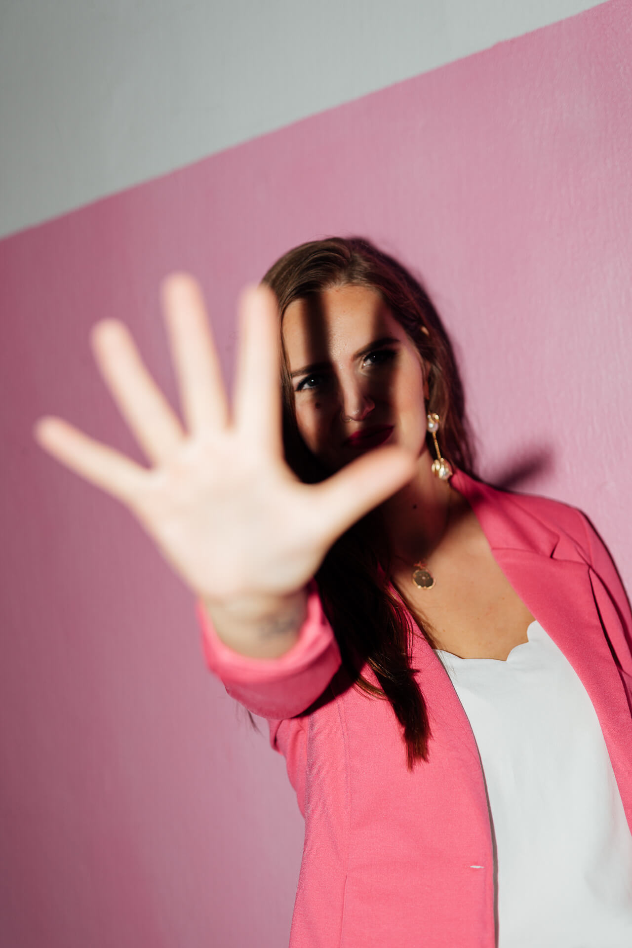 Kreatives Portrait einer Frau im pinken Blazer, die eine Hand vor die Kamera hält. So als wenn sie nicht fotografiert werden will
