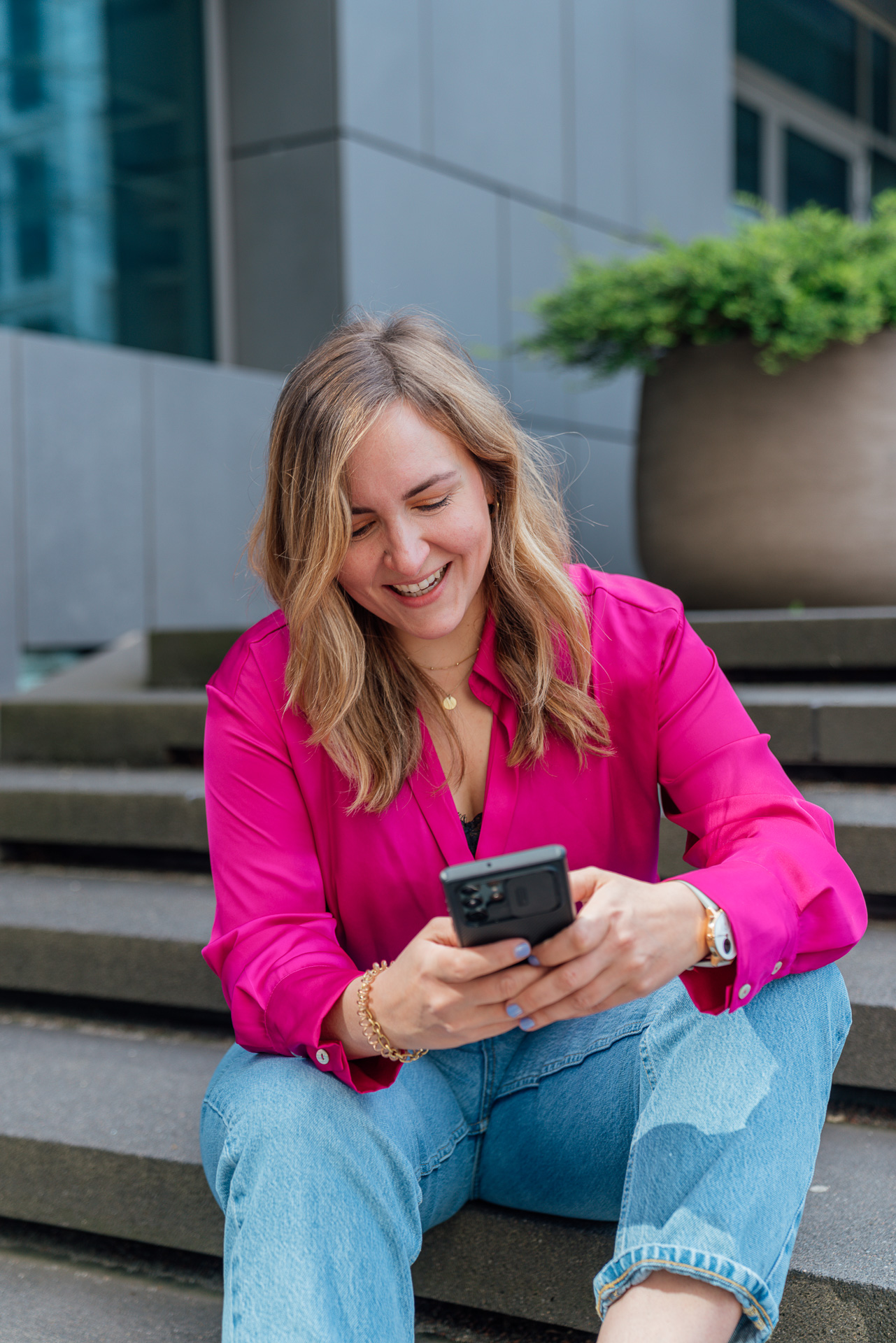 Britt sitzt auf einer schwarzen Treppe in einer pinken Bluse und tippt auf ihrem Handy rum, das Bild ist während eines Brand Shoots entstanden