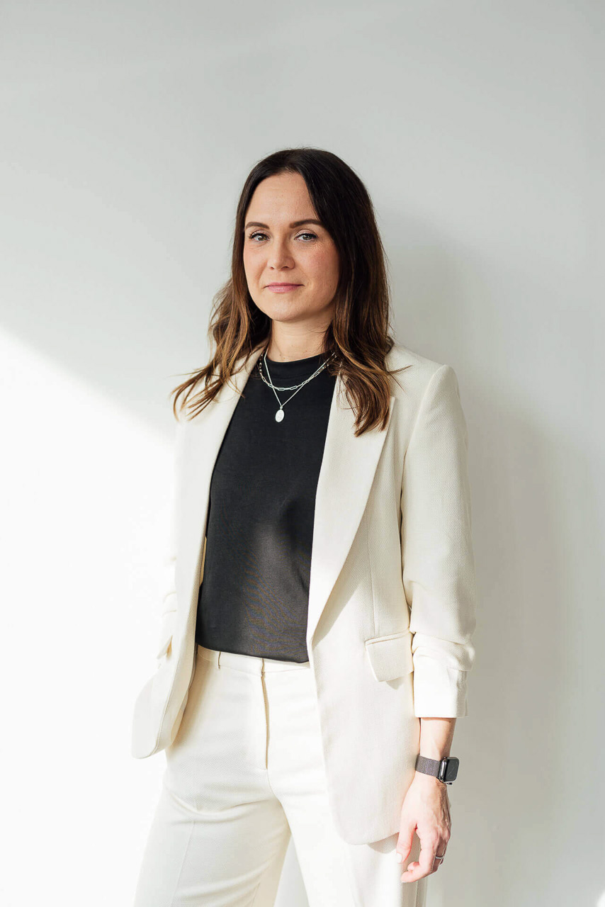 business-bilder-frauen-hamburg-1 Eine Frau die in einem langen braunen Mantel vor einer roten Mauer steht. Im Hintergrund sind Sonnenflecken an der Wand. Das Foto ist während eines Fotoshootings entstanden.