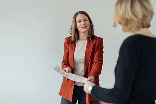 Zwei Frauen unterhalten sich und eine zeigt dabei auf ein Dokument. Das Bild ist eine authentische Arbeitssituation für ein Brand Shoot