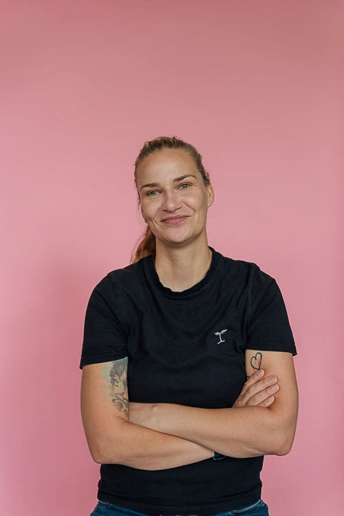 Personal-Branding-Fotos-fuer-Freelancerin-1-mobil Personal Branding Portrait einer Frau die vor einem rosafarbenen Hintergrund steht, sie lacht in die Kamera und die Arme sind verschränkt. Obwohl sie die arme verschränkt hat, ist es ein offenes und authentisches Brandingfoto