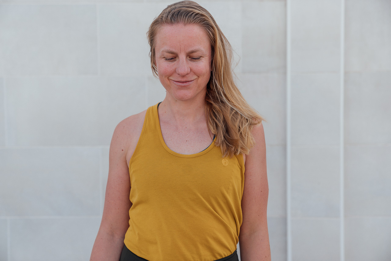 Beispielfoto-Brandingfarben-Brandshoot-1-mobil Brand Portrait einer Yogalehrerin sie steht direkt vor der Kamera, hat ein gelbes Top an und schaut nach unten. Ein schönes Beispiel, dass Businessfotos nicht immer klassisch im Balzer sein müssen