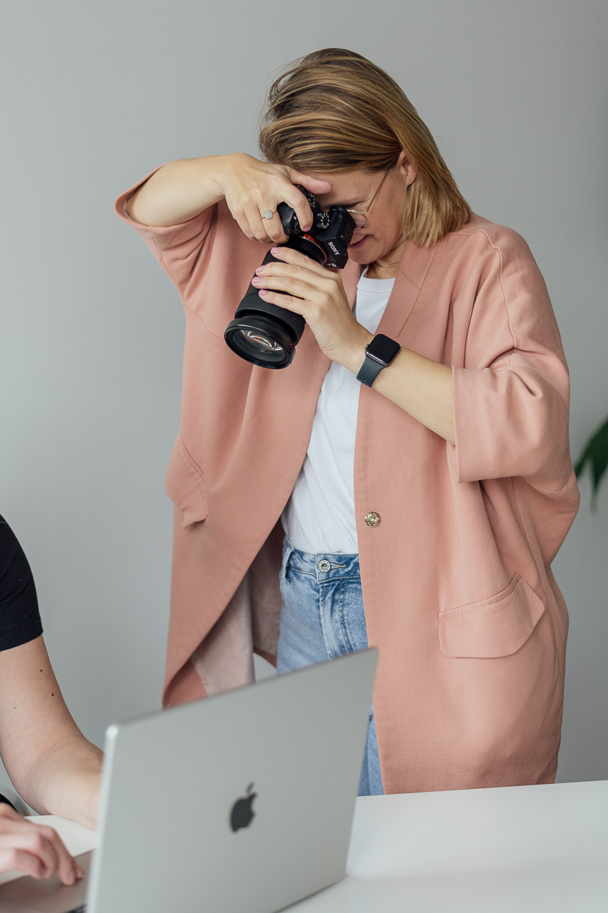 Businessfotografin-on-location-Hamburg Businessfotografin Mirjam Kilter fotografiert eine Kundin bei einem Business Shoot. Sie hat die Kamera direkt vorm Gesicht und trägt einen rosanen Blazer.