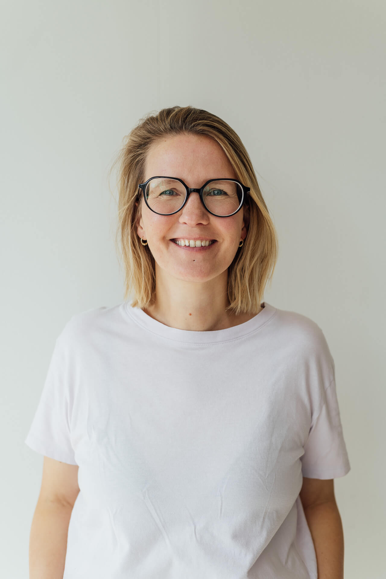 Mirjam-Kilter-Businessfotografin-fuer-authentische-Businessfotos-mobil Portrait von Businessfotografin Mirjam Kilter. Sie steht in einem lilafarbenen T-Shirt vor einer hellen Wand und schaut lächelnd in die Kamera.