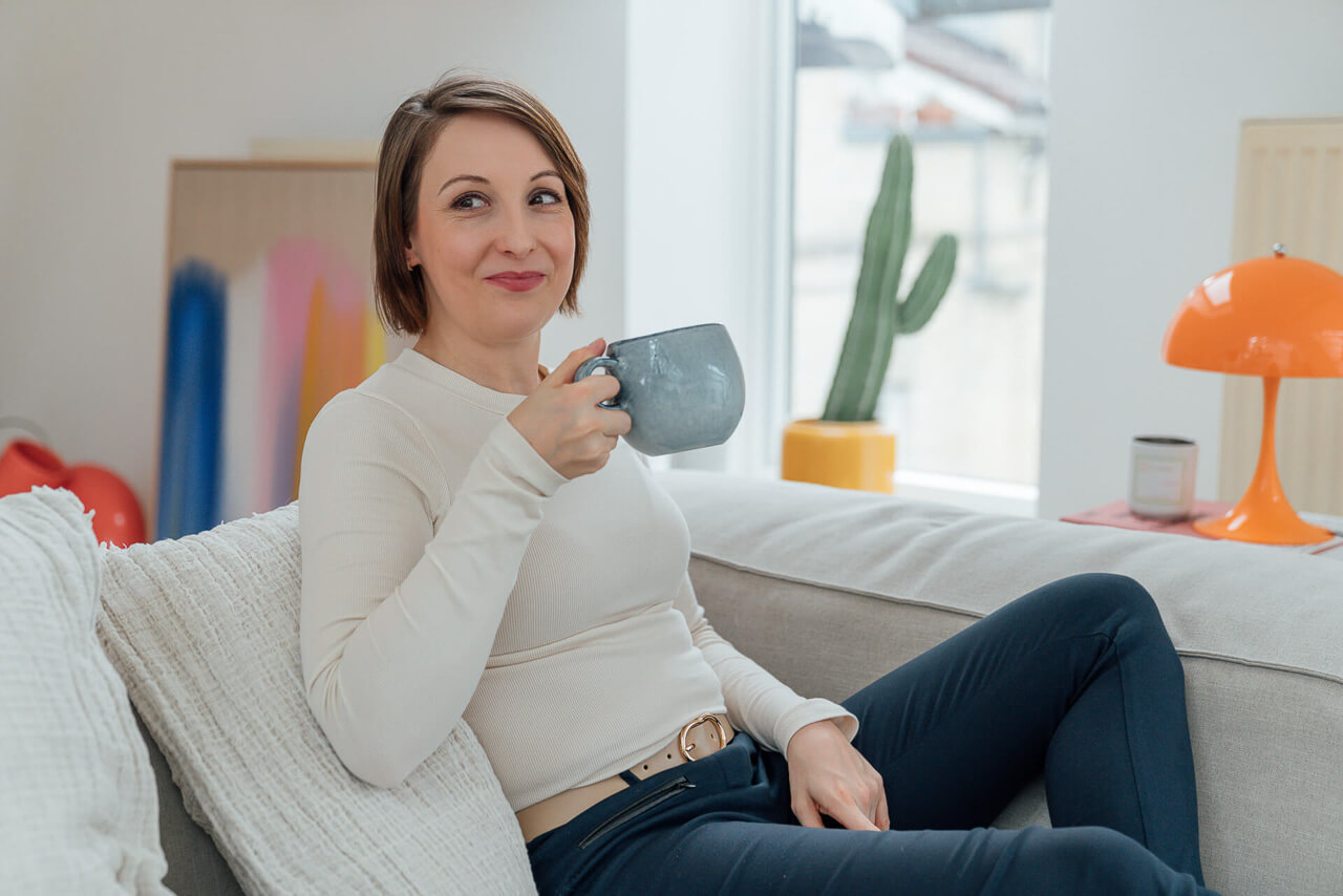 branding-fotos-oder-businessfotos-frau-mit-tasse-mobil-1 Foto einer Frau, die mit einer Tasse auf dem Sofa sitzt. Das Foto ist während eines Brand Shoots enstanden