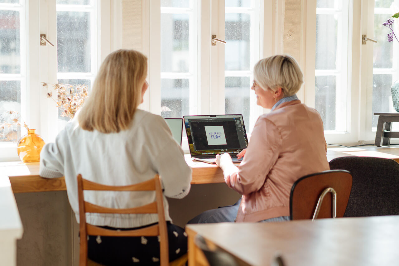 Sonja und Melanie sitzen am Schreibtisch und schauen gemeinsam in den Laptop