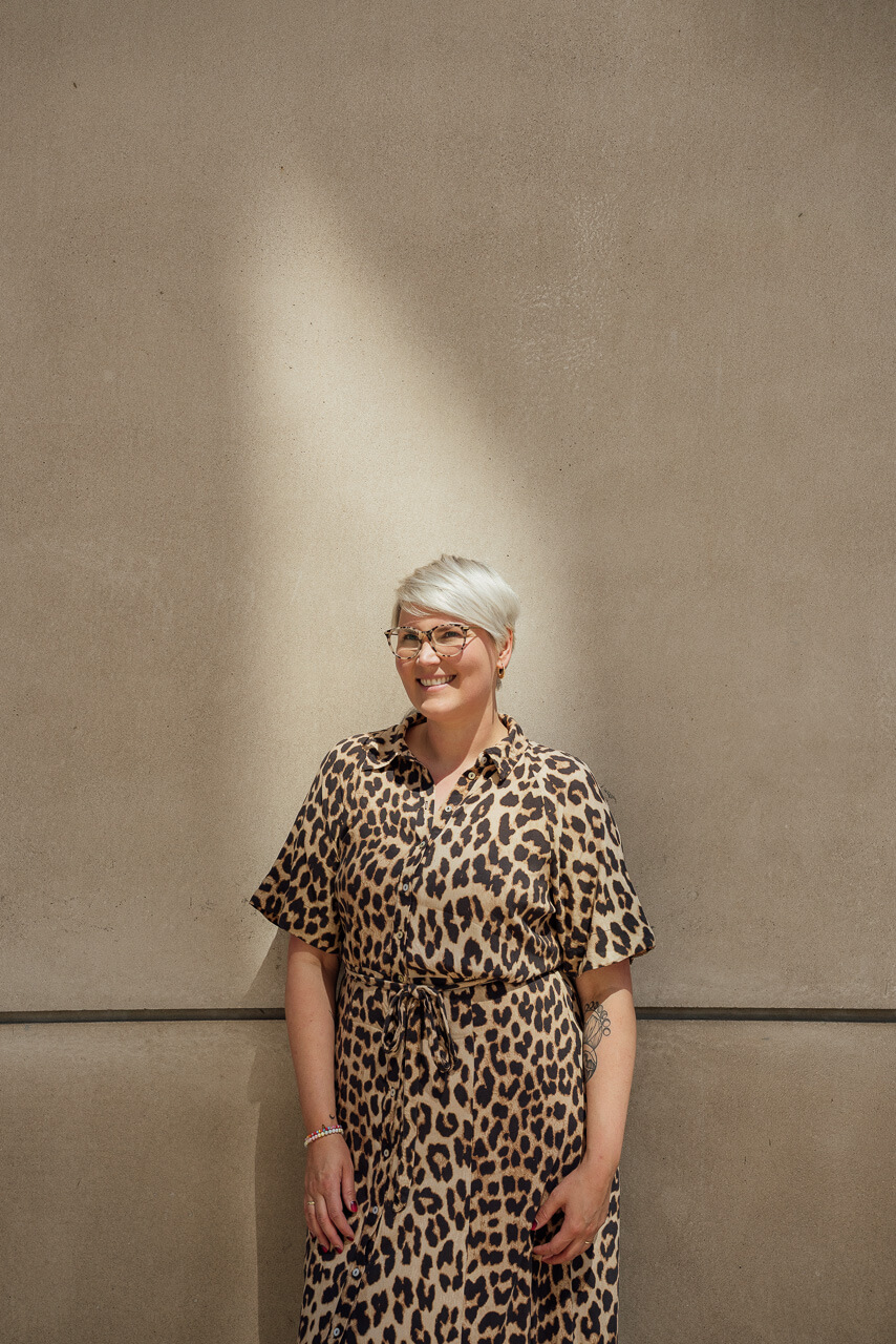 Portrait von Melanie für ihr Brand Shoot vor einer beigen Mauer und im Hintergrund sieht man ein Lichtfleck
