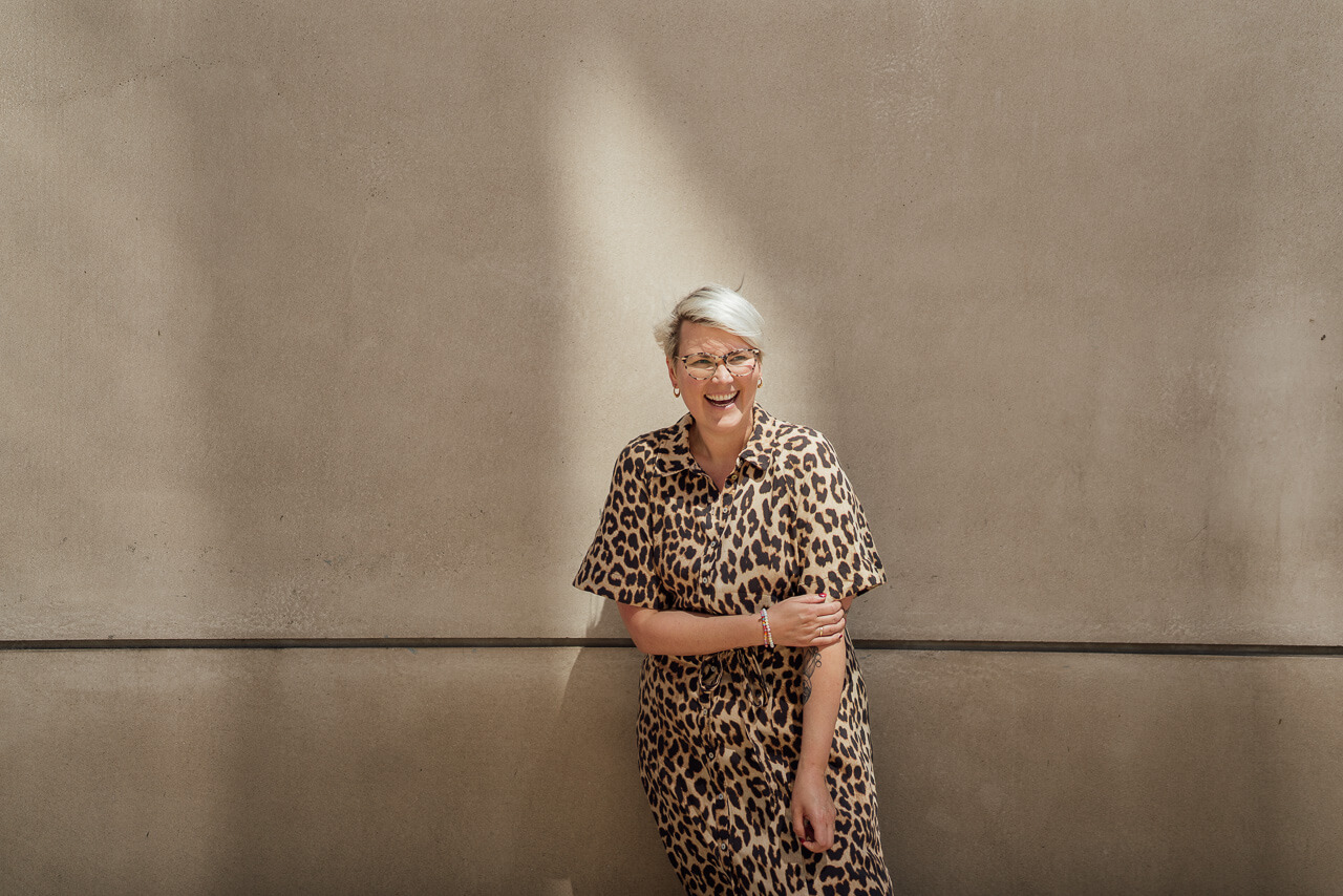 Portrait von Sonja vor einer beigen Mauer mit einem Lichtfleck im Hintergrund