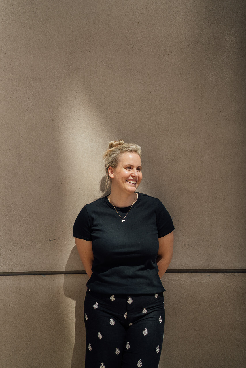 Portrait von Sonja für ihr Brand Shoot vor einer beigen Mauer und im Hintergrund sieht man ein Lichtfleck