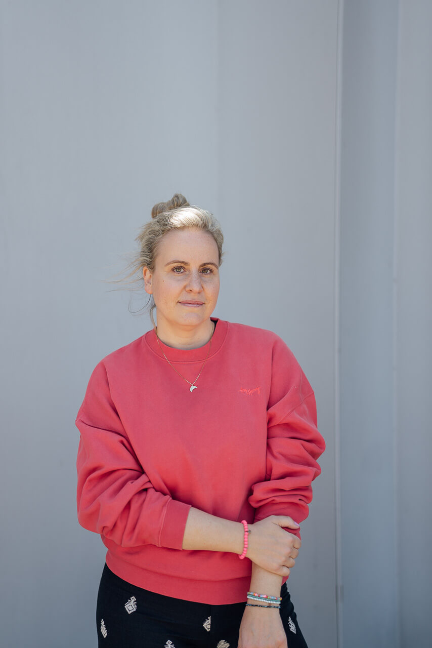 Portrait von Sonja von Schockverliebt vor einer grauen Mauer in rotem Pulli. Das Bild ist für ein Brand Shoot