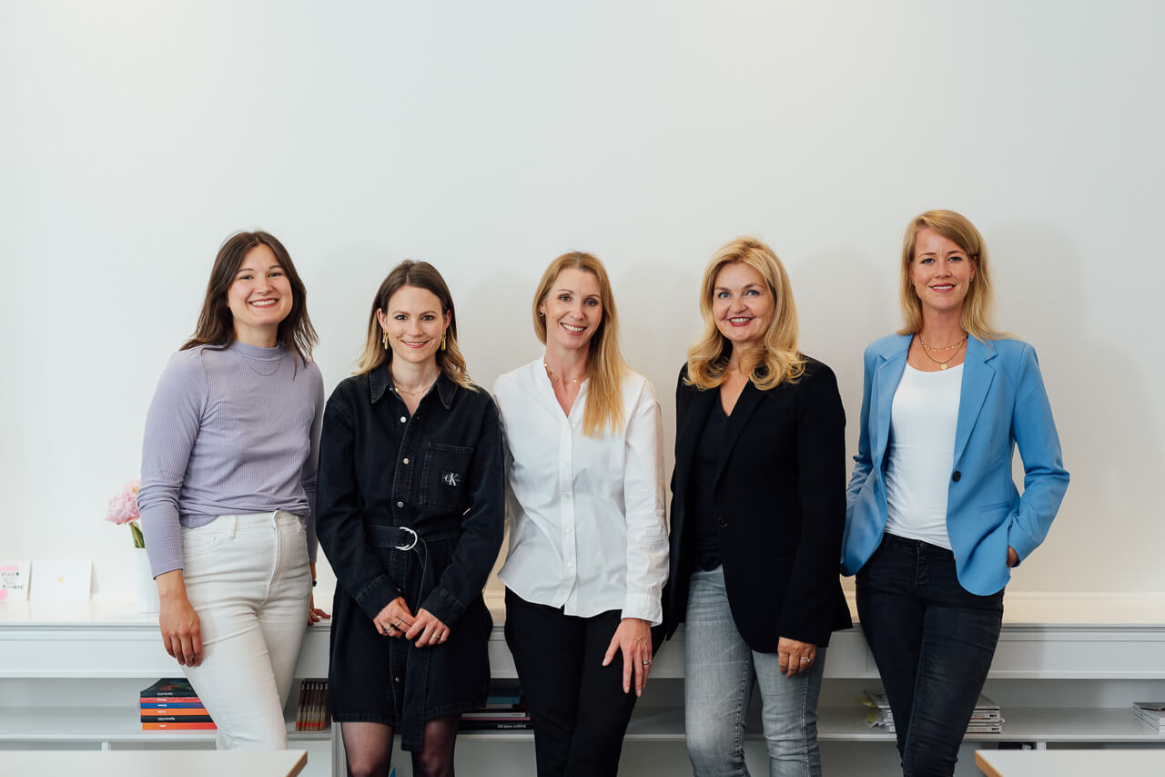 Teamfoto mit fünf Personen, sie stehen alle nebeneinander und lehnen an einem Sidboard. 