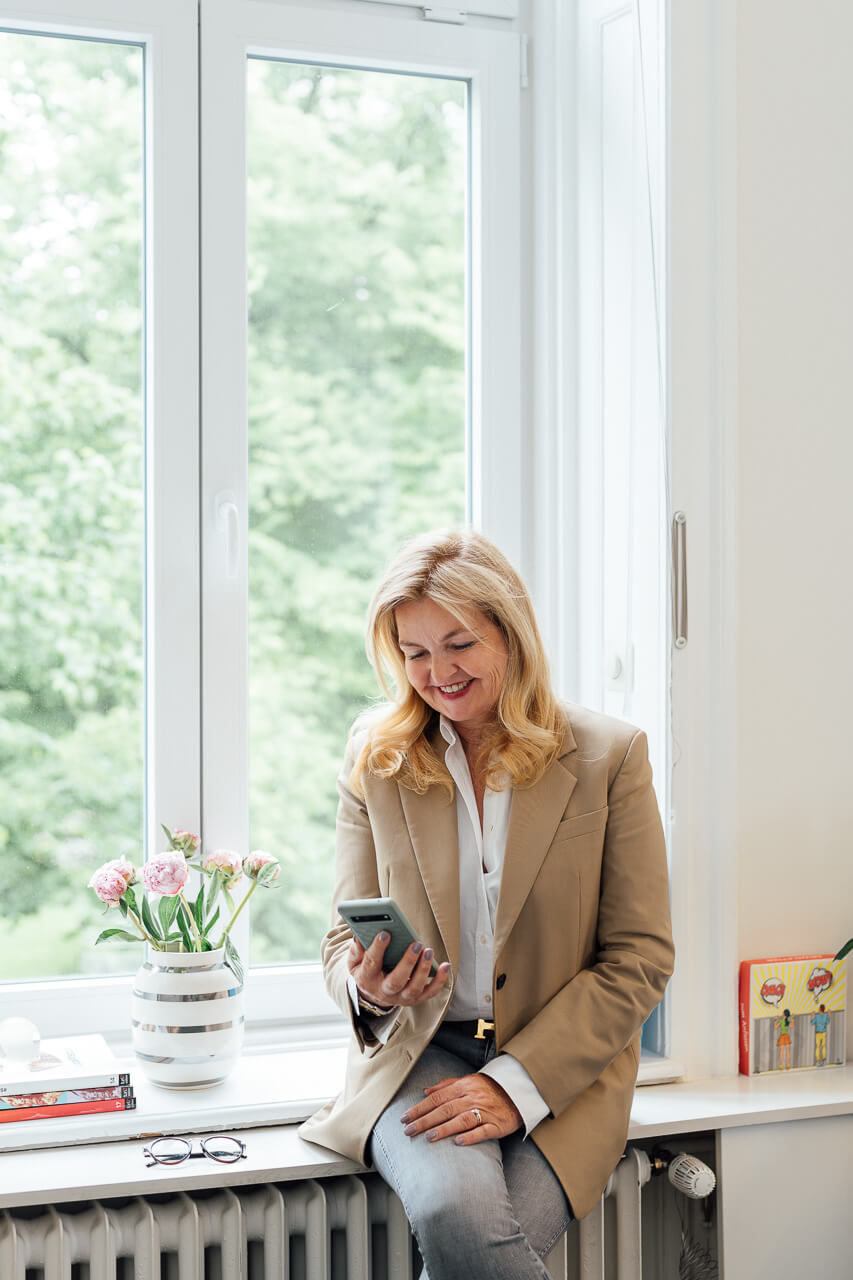 Portrait einer Frau, die auf einer Fensterbank sitzt und in ihr Handy schaut. Das Bild ist während eines Corporate Shooting entstanden