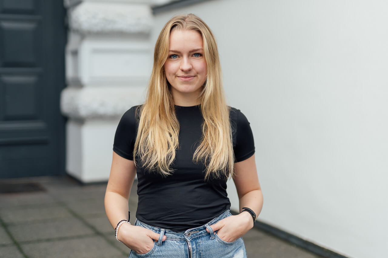 Authentisches Mitarbeiterportrait einer Frau, die vor einer weißen Mauer steht