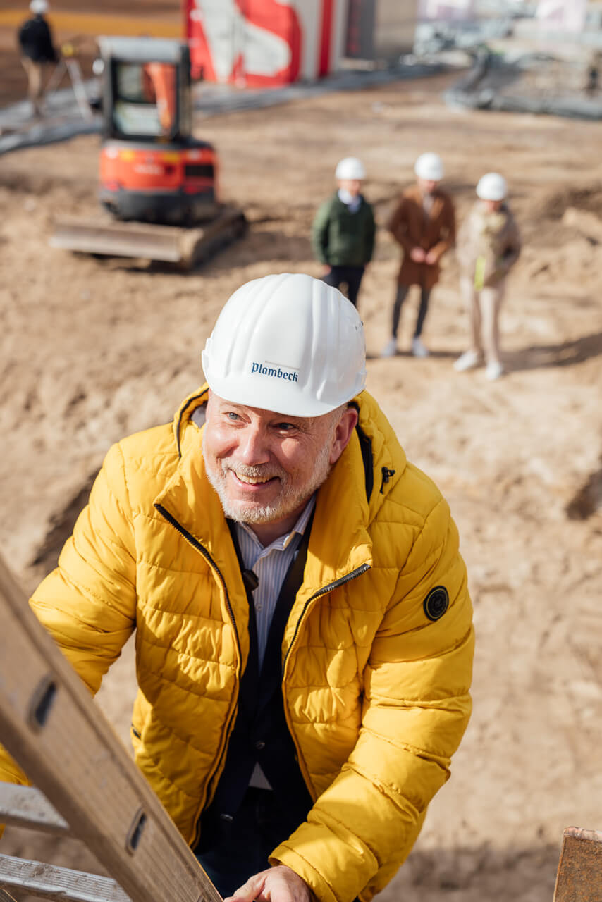 Der Bürgermeister von Plambeck steigt in die Baugrube auf einer Leiter hinab