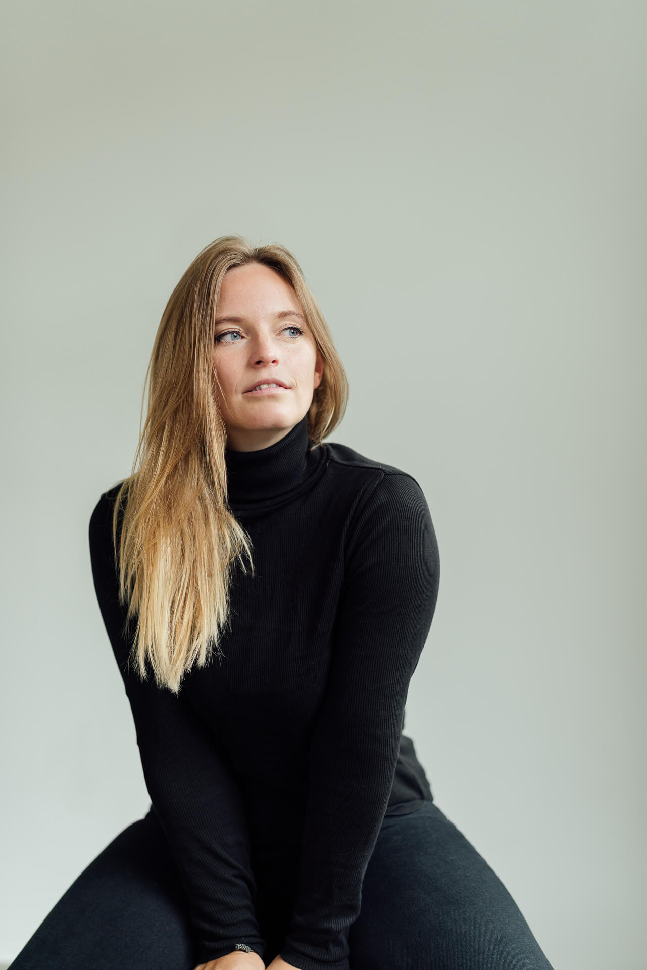 Studio-Days-Hamburg-Beispielbild-Anne-1 Portrait von Anne, die auf einem Hocker sitzt und leicht zur Seite schaut. Sie hat ein schwarzes Outift an