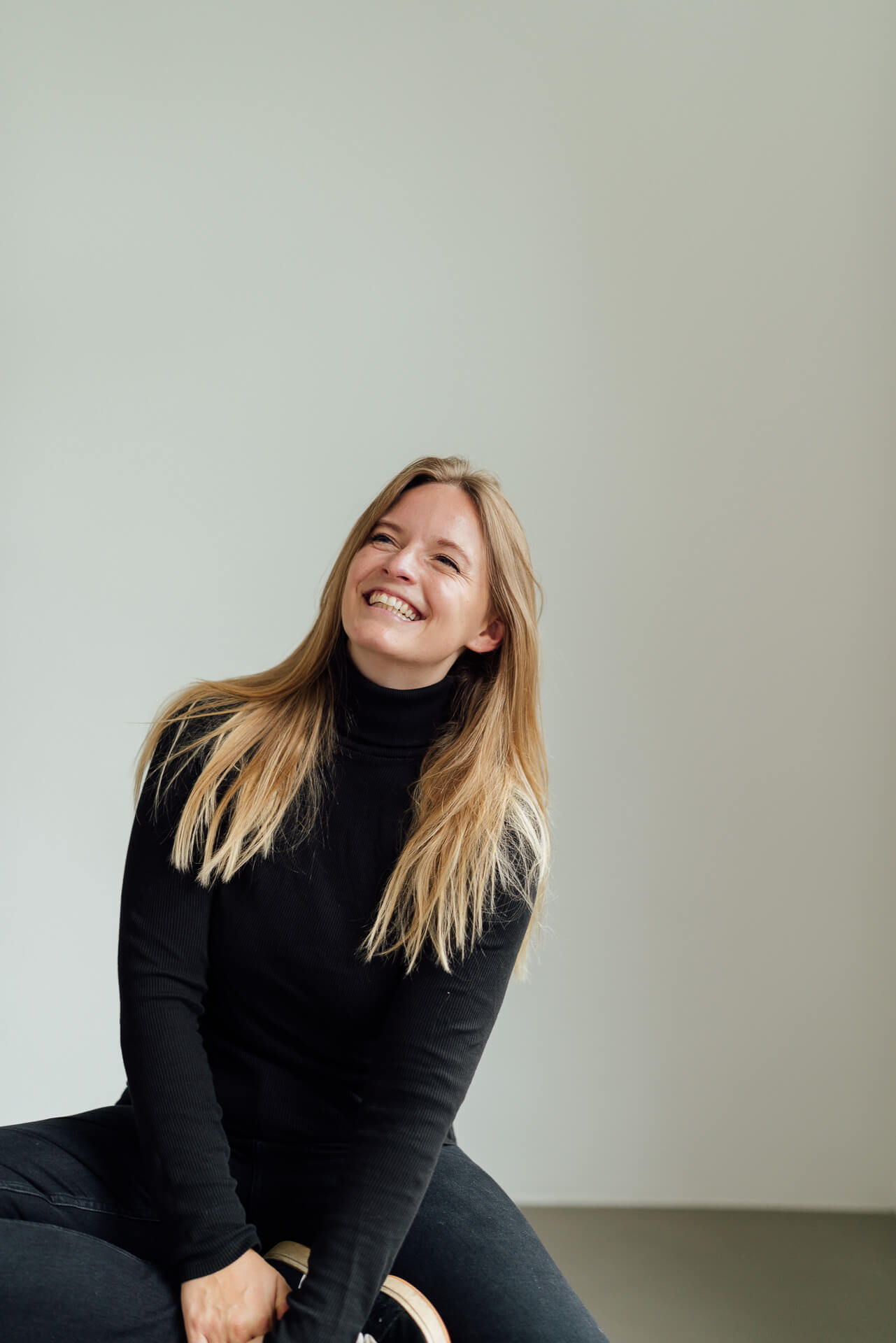 Studio-Days-Hamburg-Beispielbild-Anne Eine Frau im schwarzen Outfit sitzt auf einem Hocker und schaut lachend in die Kamera