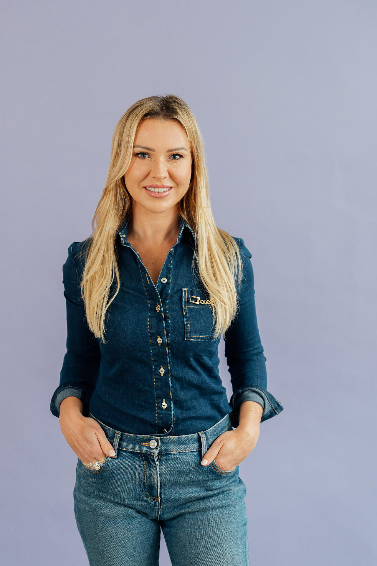Studio-Days-Hamburg-Beispielbild-Karo Eine Frau in Jeans und Jeansbluse steht vor einem lila Hintergrund und lächelt in die Kamera.