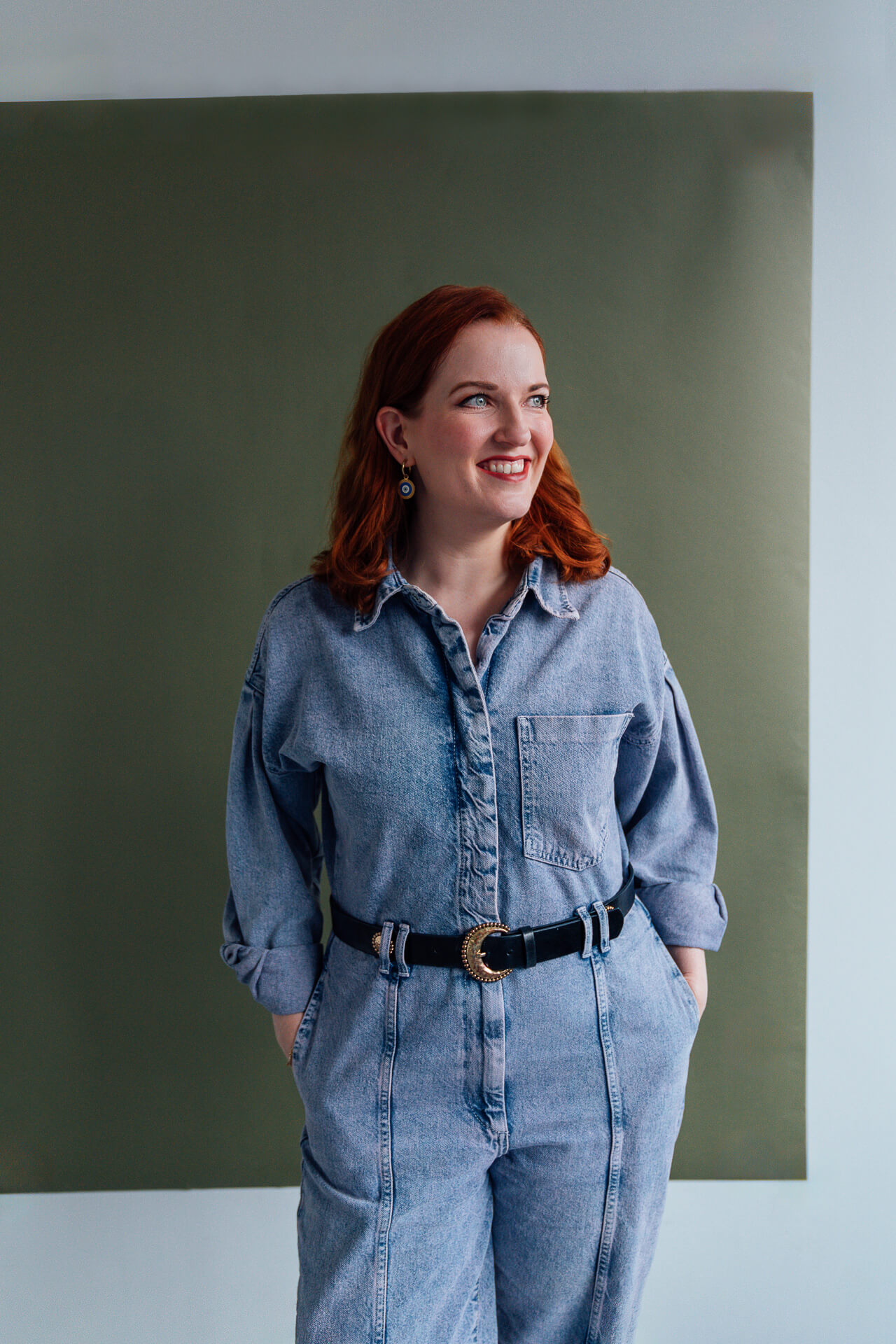 Studio-Days-Hamburg-Beispielbild-vor-gruen Portrait einer Frau, die in einem Hosenanzug aus Jeans vor einem grünen Hintergrund steht und leicht zur Seite lächelt