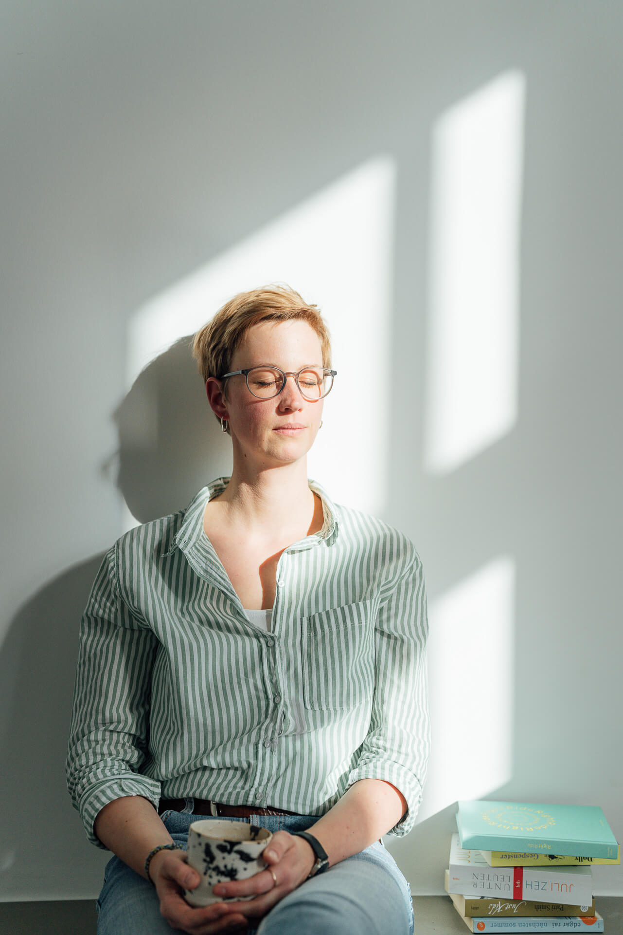 Studio-Days-Hamburg-Portrait-Shooting-Franzi Eine Frau sitzt mit geschlossenen Augen angelehnt an eine Wand. Sie schaut entspannt und sie hat eine Tasse in der Hand