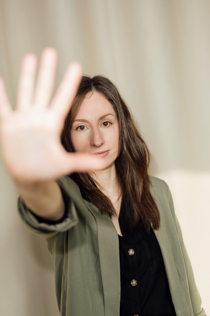 Studio-Days-Hamburg-Portrait-Shooting-Nicole Studioportraits einer Frau die vor einem beigen Hintergrund steht, sie hält die Hand zur Kamera wie eine Art Stop Zeichen