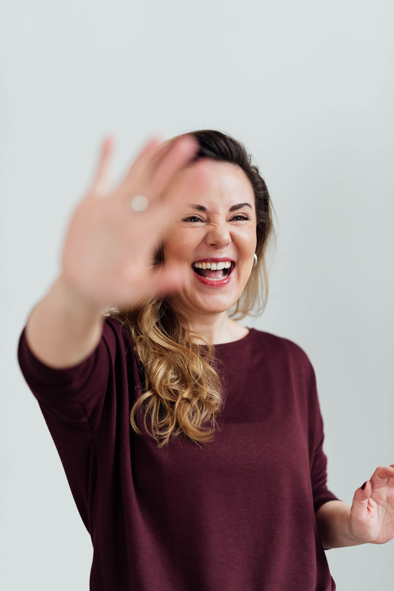 Eine Frau im schwarzen Outfit sitzt auf einem Hocker und schaut lachend in die Kamera