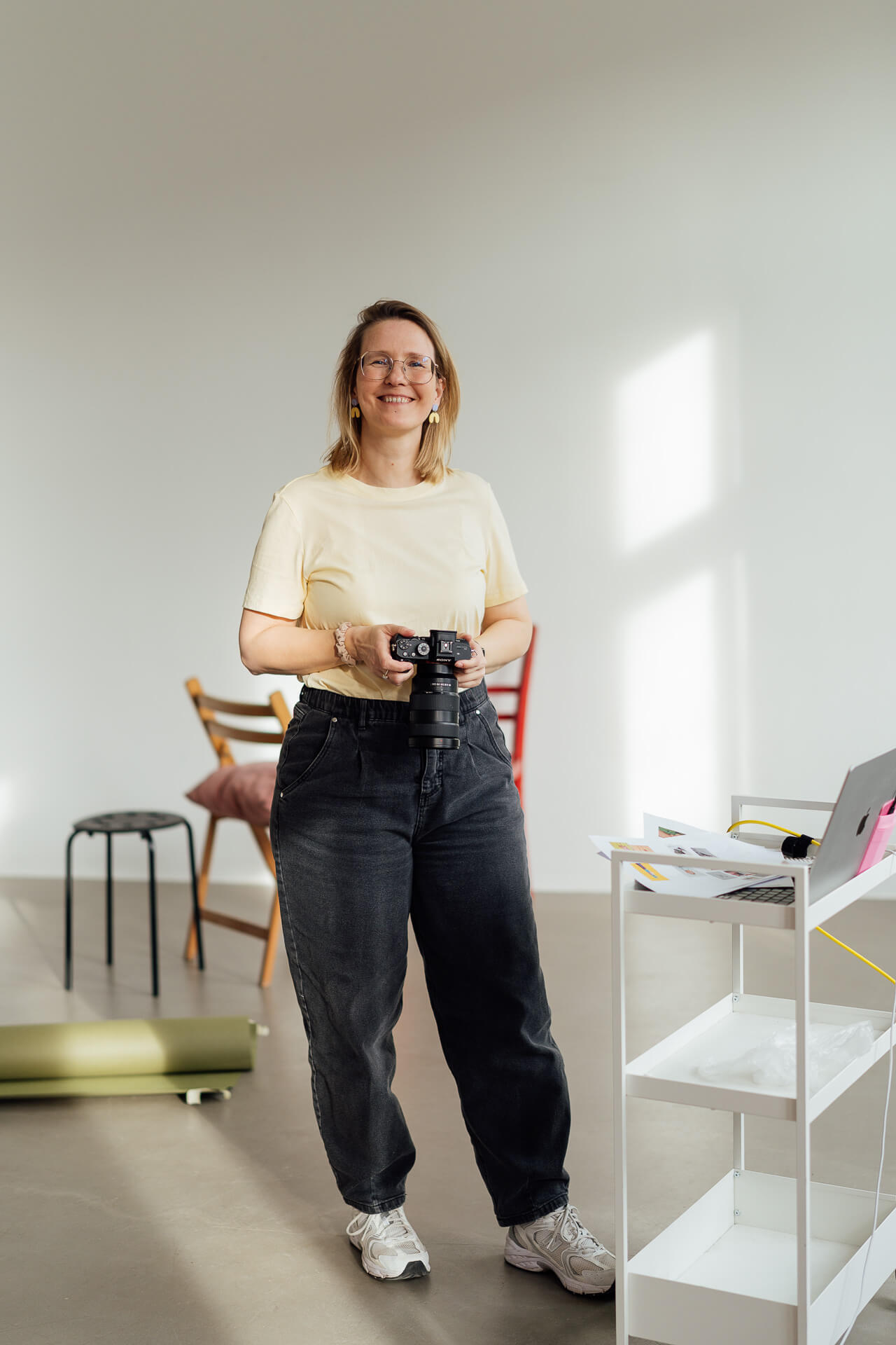Personal Branding Fotografin Mirjam Kilter steht im Tageslichtstudio mit einer Kamera und lächelt in die Kamera