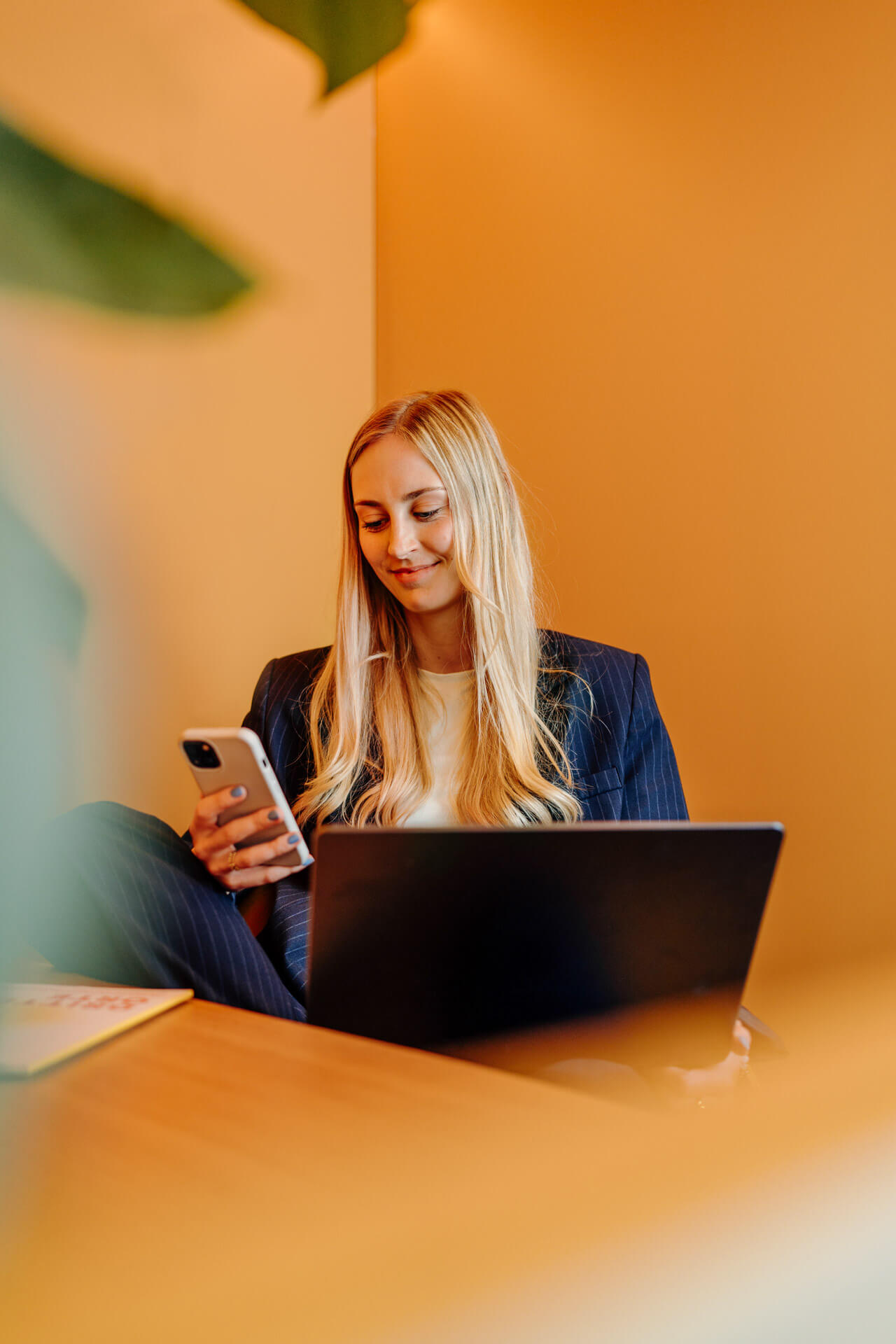 Businessfotografie-Hamburg-Businessportrait-Frau Portrait einer Frau die in einem gelben Häuschen sitzt und lächelnd aufs Handy schaut, sie hat dabei einen Laptop auf dem Schoss. Das Bild ist im Rahmen eines Fotoshootings für neue Imagebilder eines Unternehmens entstanden