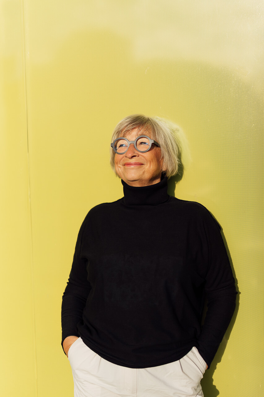 Businessportrait einer Frau im schwarzen Pullover vor einer knallgelben Wand, sie schaut dabei leicht zur Seite