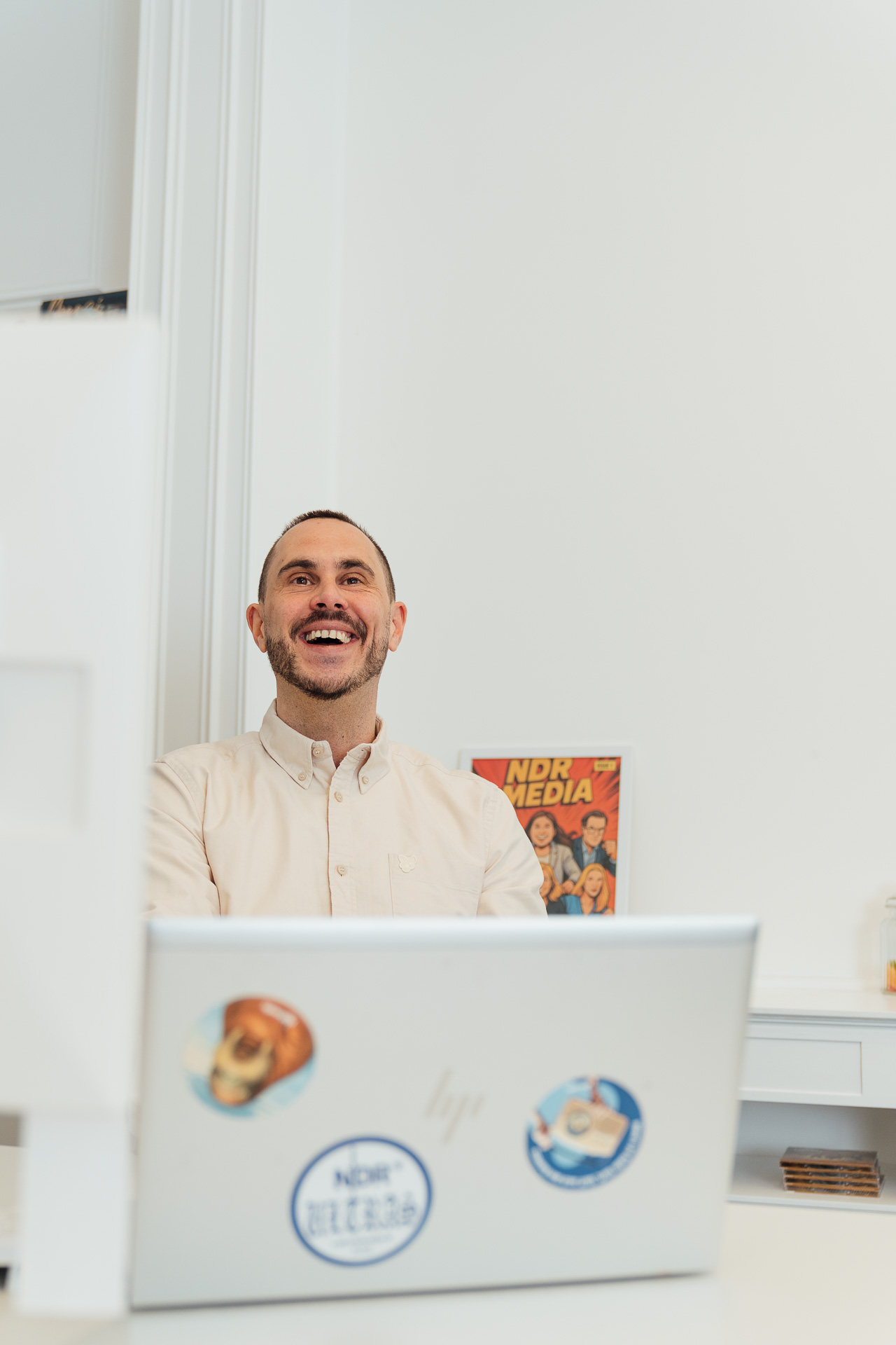 Ein Mitarbeiter sitzt hinter seinem Laptop und schaut lachend zu einem Kollegen, der aber nicht im Bild ist. Das Bild ist von der Businessfotografin Mirjam Kilter