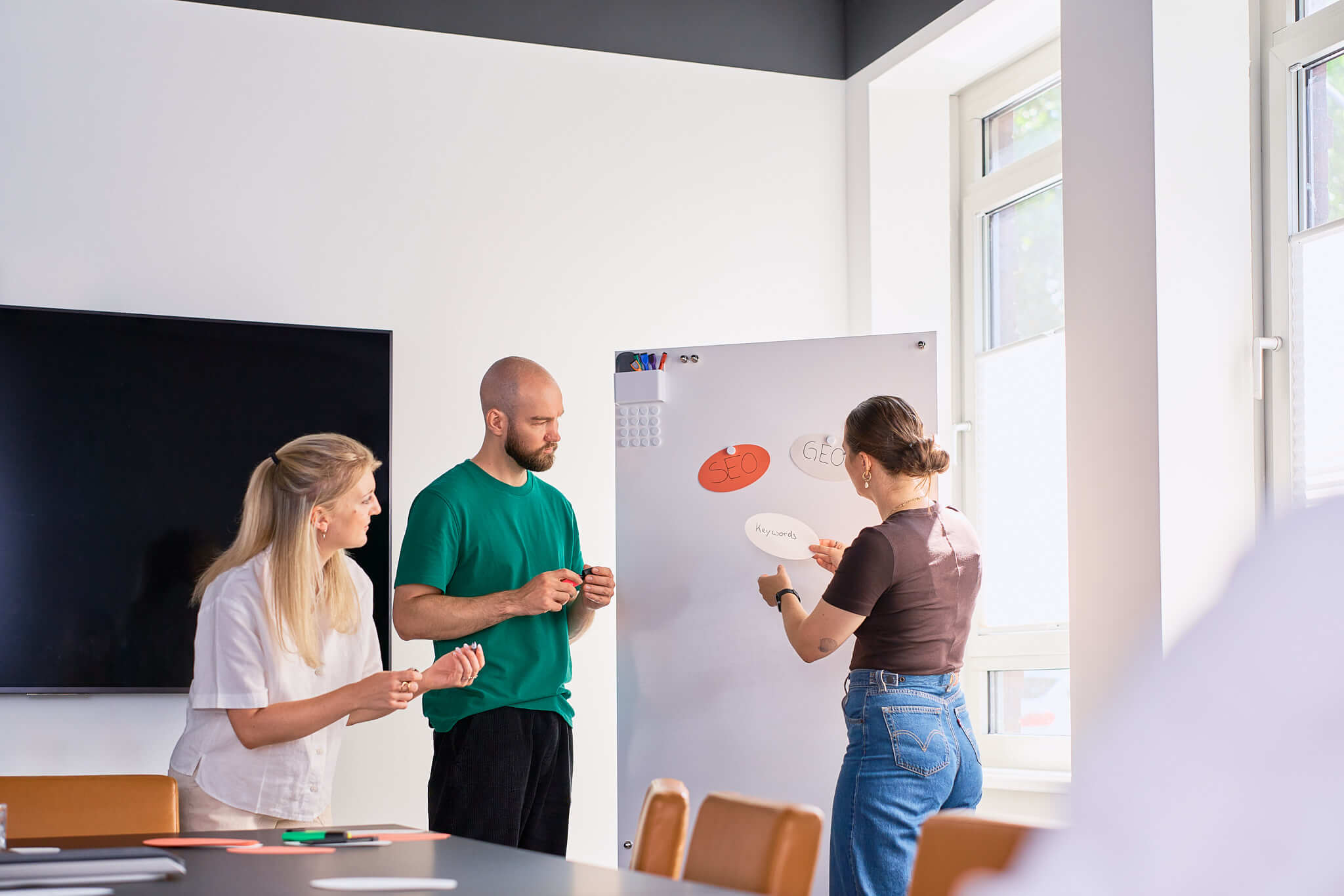 businessfotos-seo-agentur-meetingsituation-am-whiteboard Meeting-Szene mit drei Mitarbeitenden einer SEO-Agentur am Whiteboard