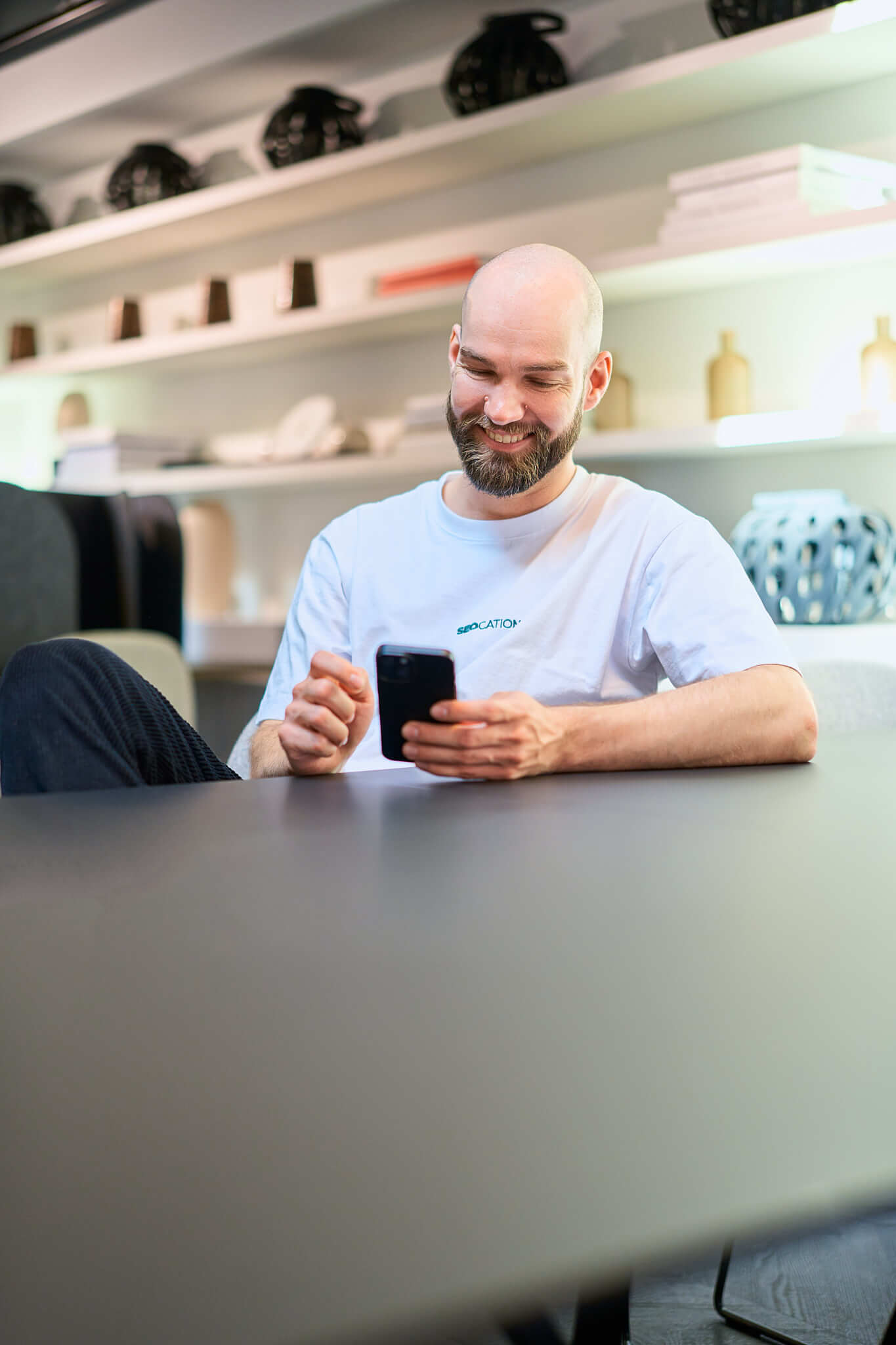 businessfotos-seo-blick-ins-handy Portrait einer Frau die in einem gelben Häuschen sitzt und lächelnd aufs Handy schaut, sie hat dabei einen Laptop auf dem Schoss. Das Bild ist im Rahmen eines Fotoshootings für neue Imagebilder eines Unternehmens entstanden